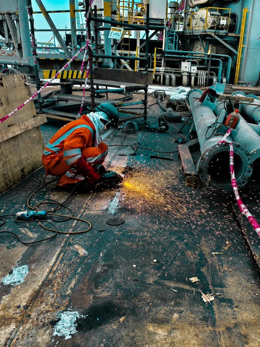 Worker in an orange flame-resistant coverall grinding metal with sparks