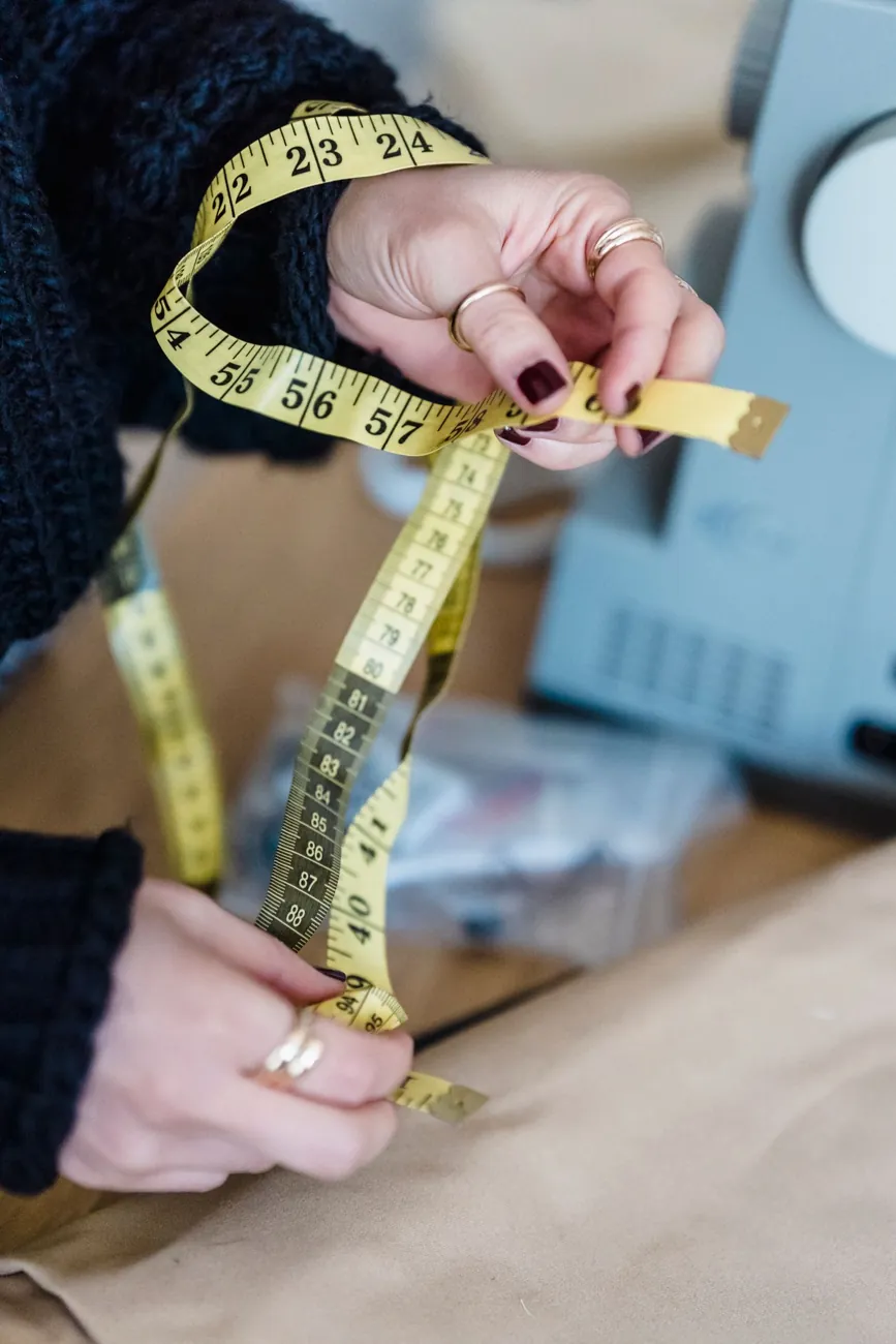 Hands pulling a yellow measuring tape taut beside a sewing machine