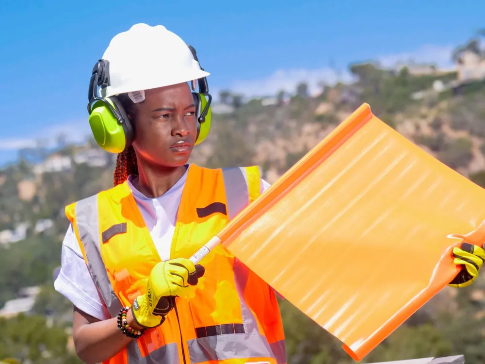 Worker in an orange reflective vest and hard hat holding a signalling flag